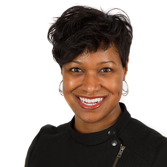 A person smiles widely while wearing a black top with button details. The background is a plain white, highlighting the individual and creating a clean, professional look.
