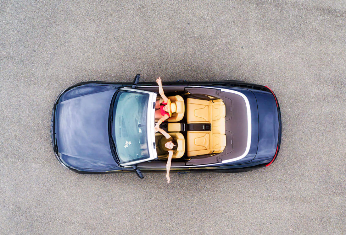 Overhead view of a black convertible with tan seats on a road, two people inside.