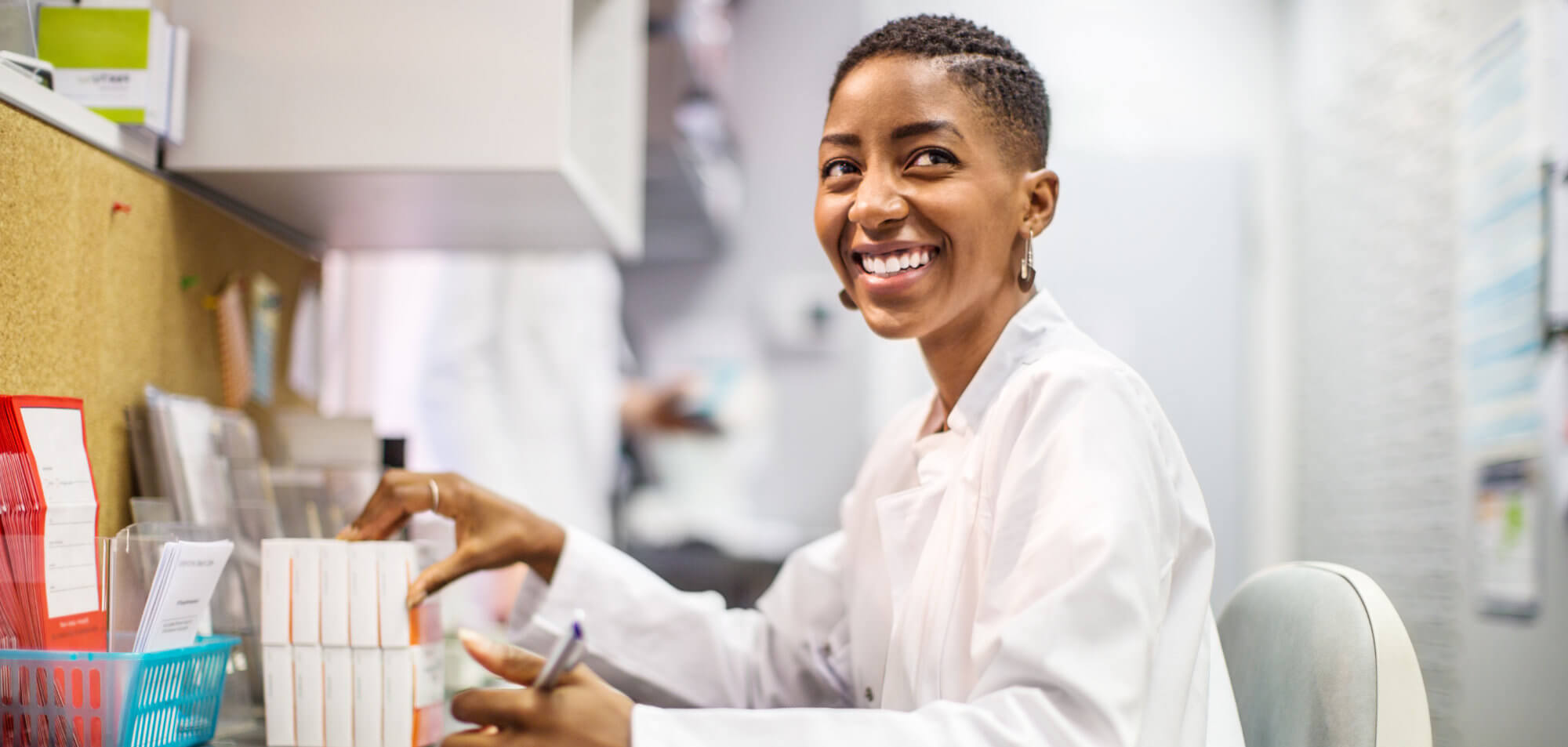 Smiling professional in a white coat, organizing documents in a bright office.