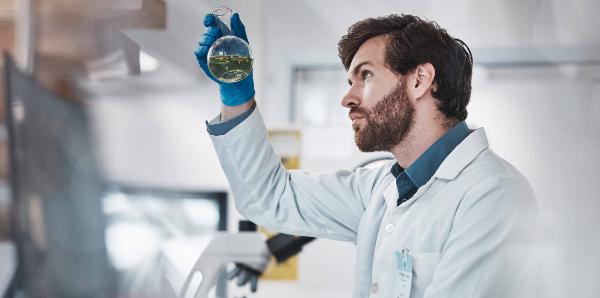 Scientist in a lab coat examining a green liquid in a beaker, demonstrating innovation.