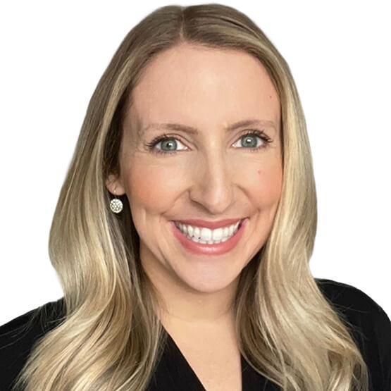 Blonde woman smiles broadly at camera, showing teeth; wearing a black top and round sparkly stud earrings; long wavy hair frames her face against a plain white background.