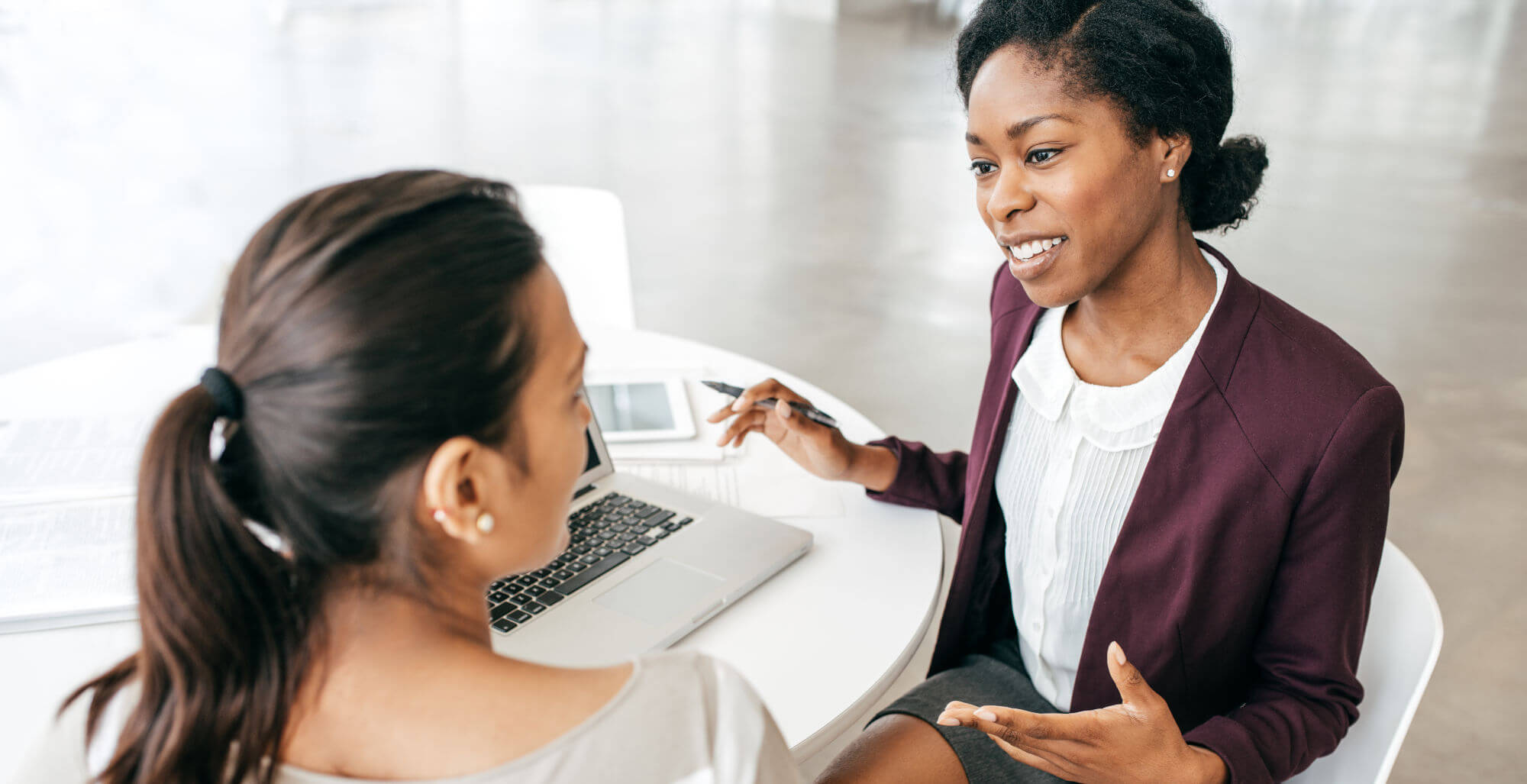 Two women sitting at a table with a laptop on it.
