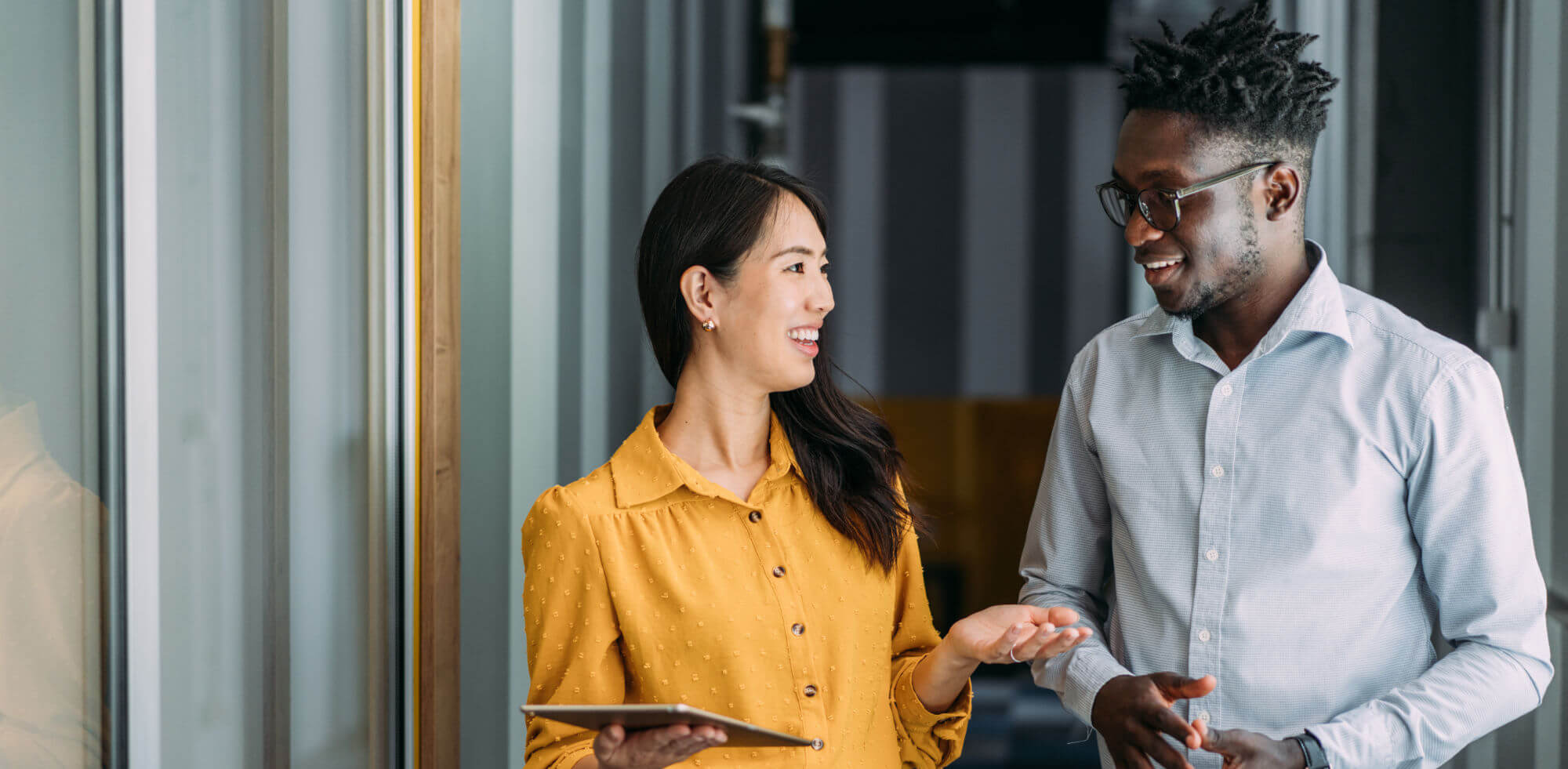 Shot of a two confident business persons talking in the work place. Two colleagues using a digital tablet while walking in a modern office. Businessman and businesswoman in meeting discussing business strategy. Business coworkers working together in the office.