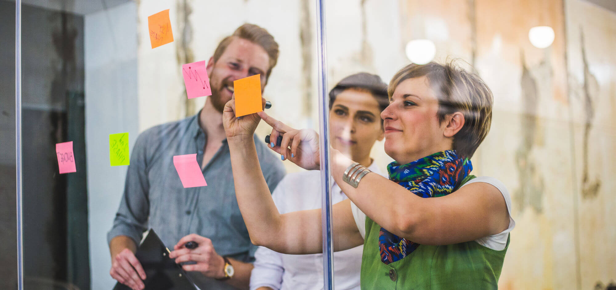 Young business people ideating with sticky notes on a glass wall.
