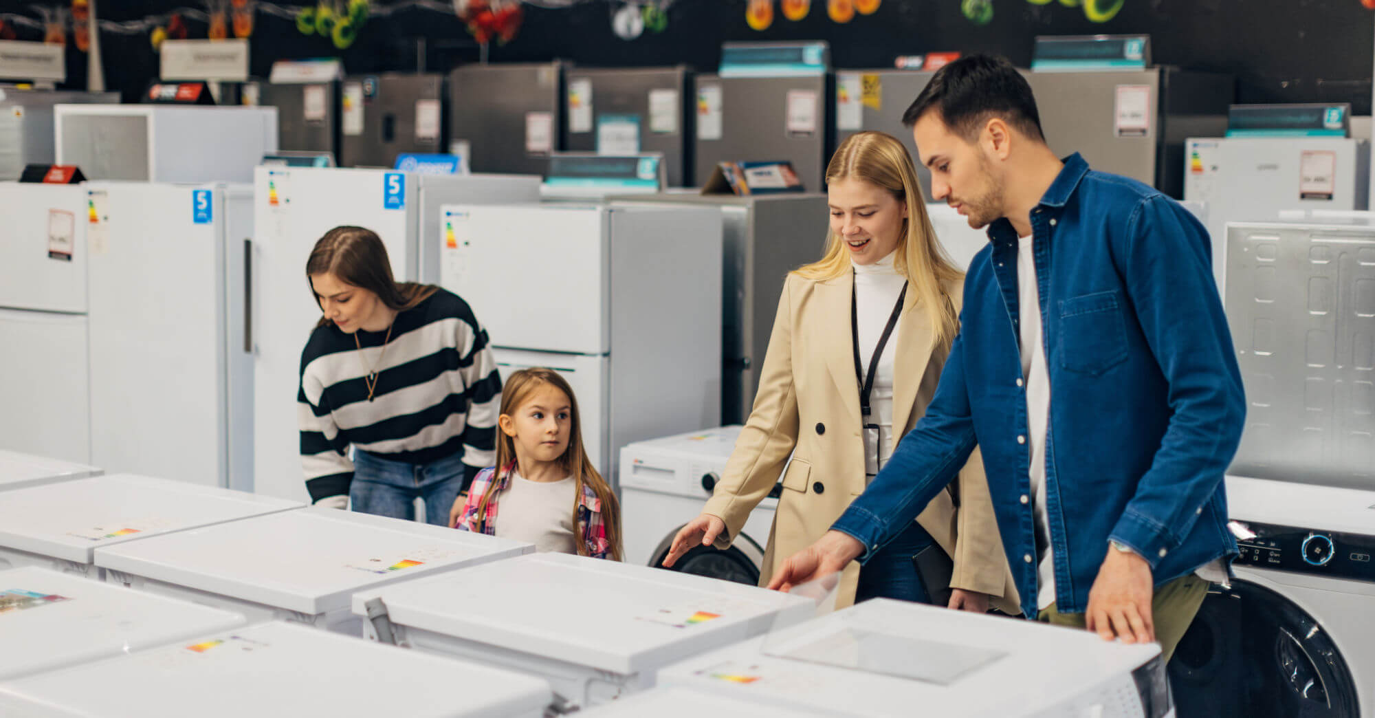 People examining appliances in a showroom, featuring white refrigerators.