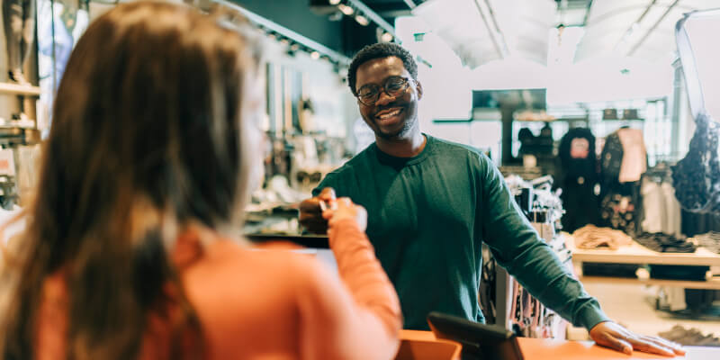 Cashier smiling as a customer hands over a payment card at the counter.