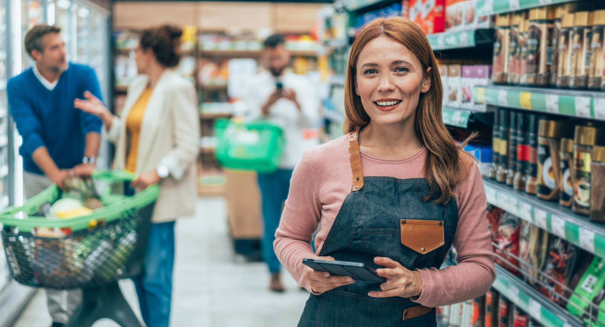 Proud supermarket female employee standing and smiling at the camera. She is holding digital tablet in her hands. Shot of a young woman using a tablet at work in a supermarket.