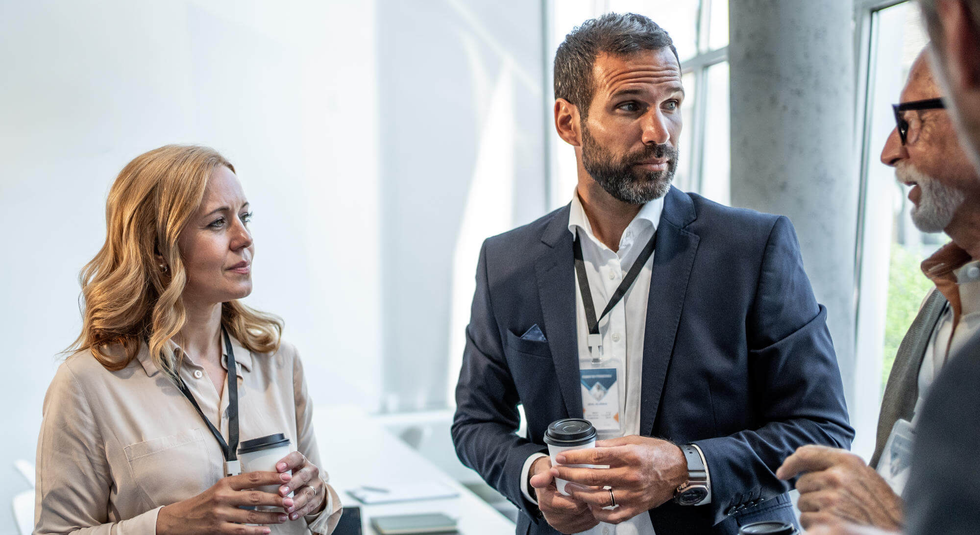 Three professionals chatting over coffee during a conference break.