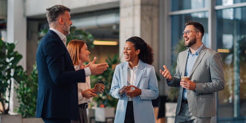 Four businesspeople talking and laughing together in the office building.