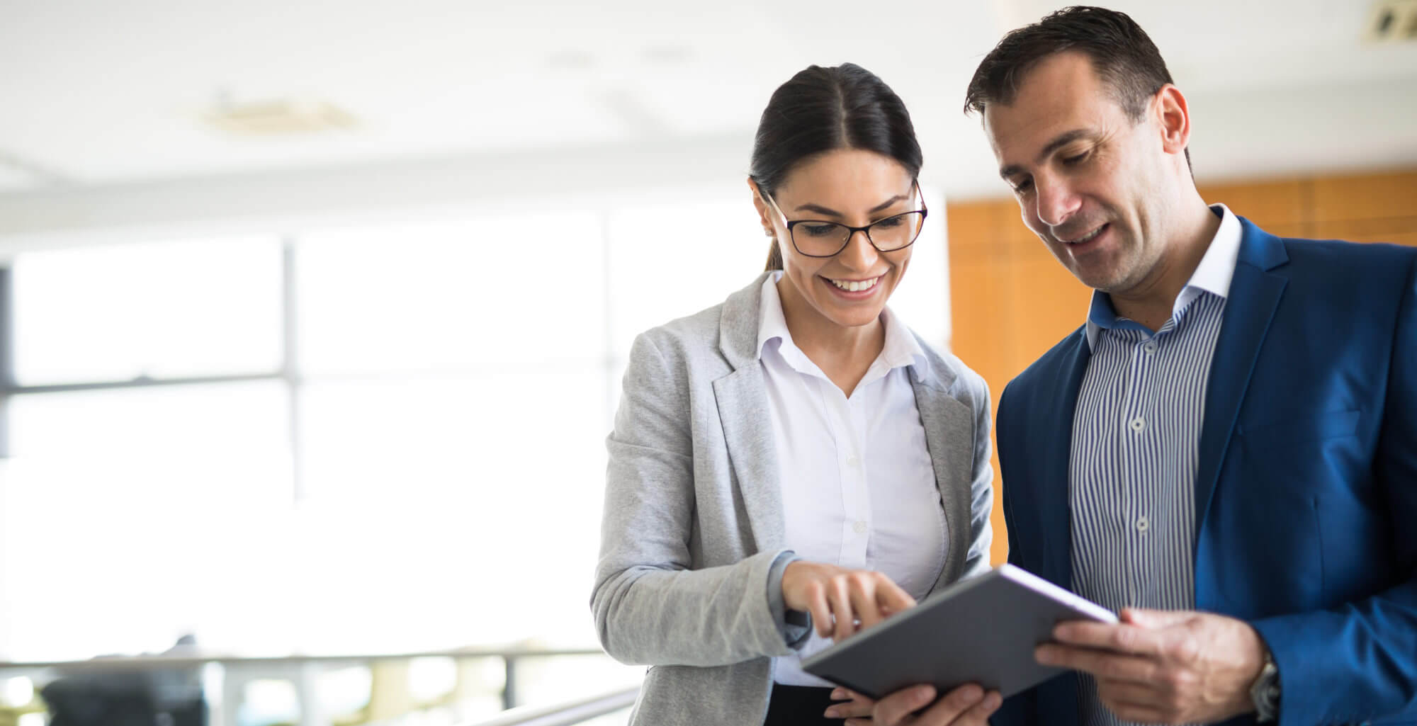 Two mixed-age business people are discussing business strategy in the office building hallway using digital tablet. Front view. Copy space.