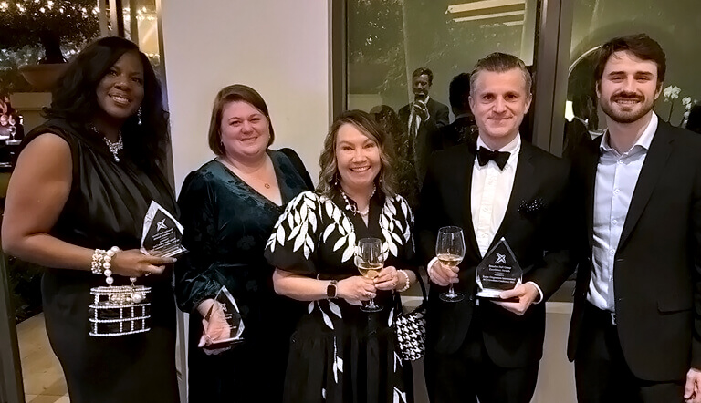 A group of people at an awards gala. Three people are holding glass trophies.