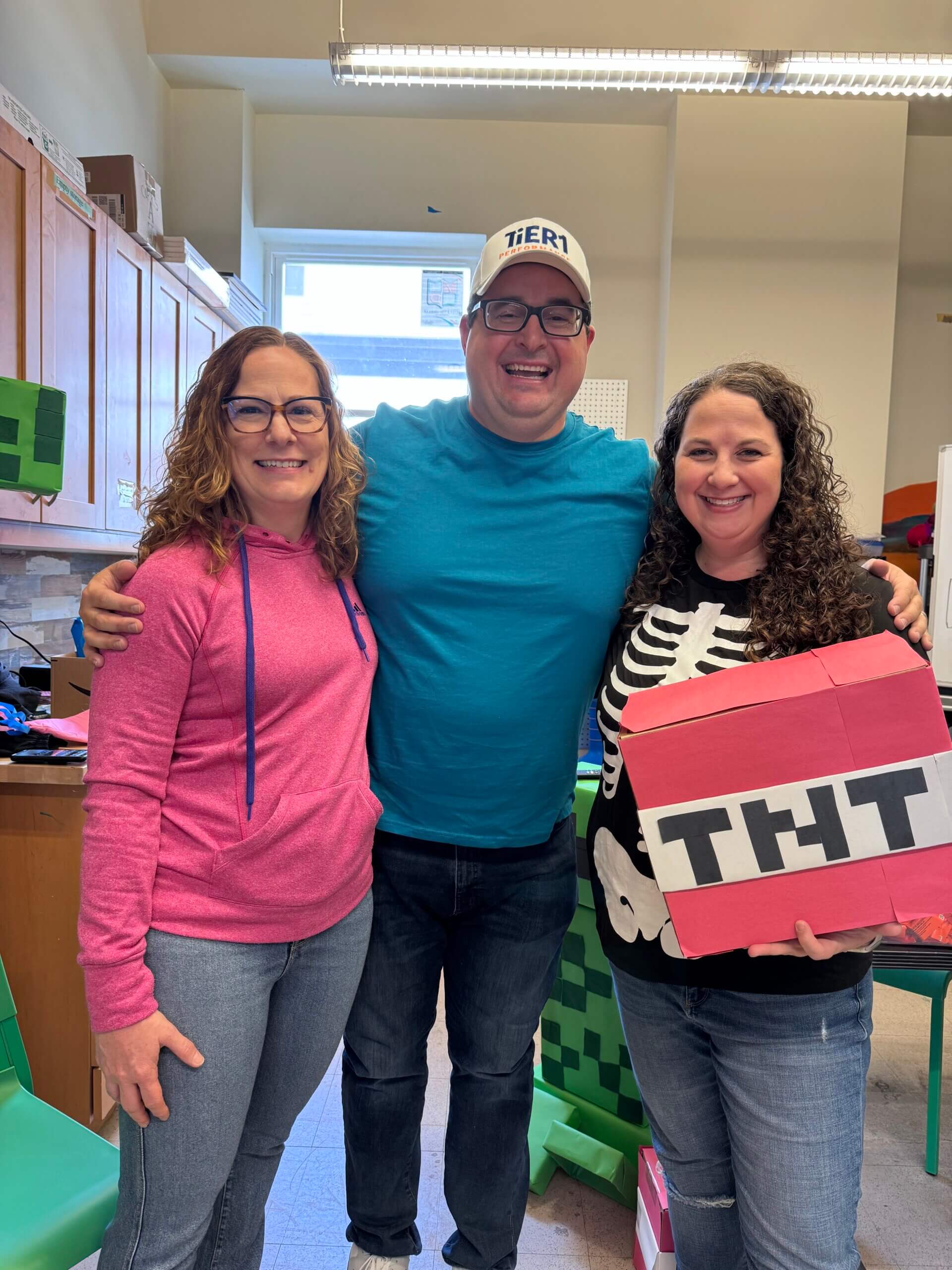Three people volunteering at a Halloween event. Their theme is Minecraft and one woman is holding a box that says TNT.
