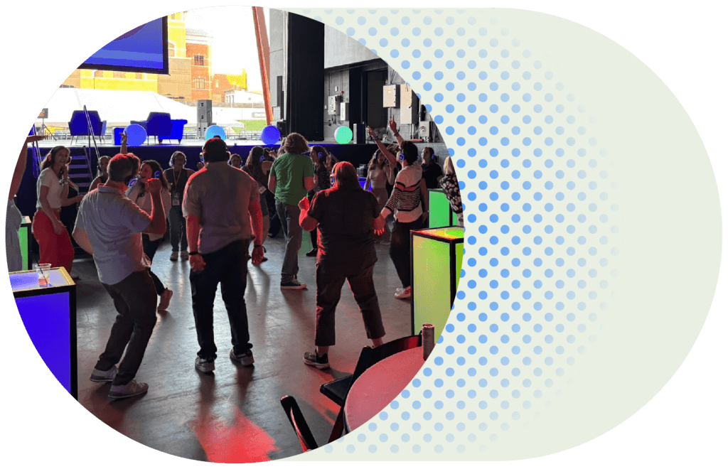 Group of people dancing together at an indoor event with colorful lighting and glowing tables.