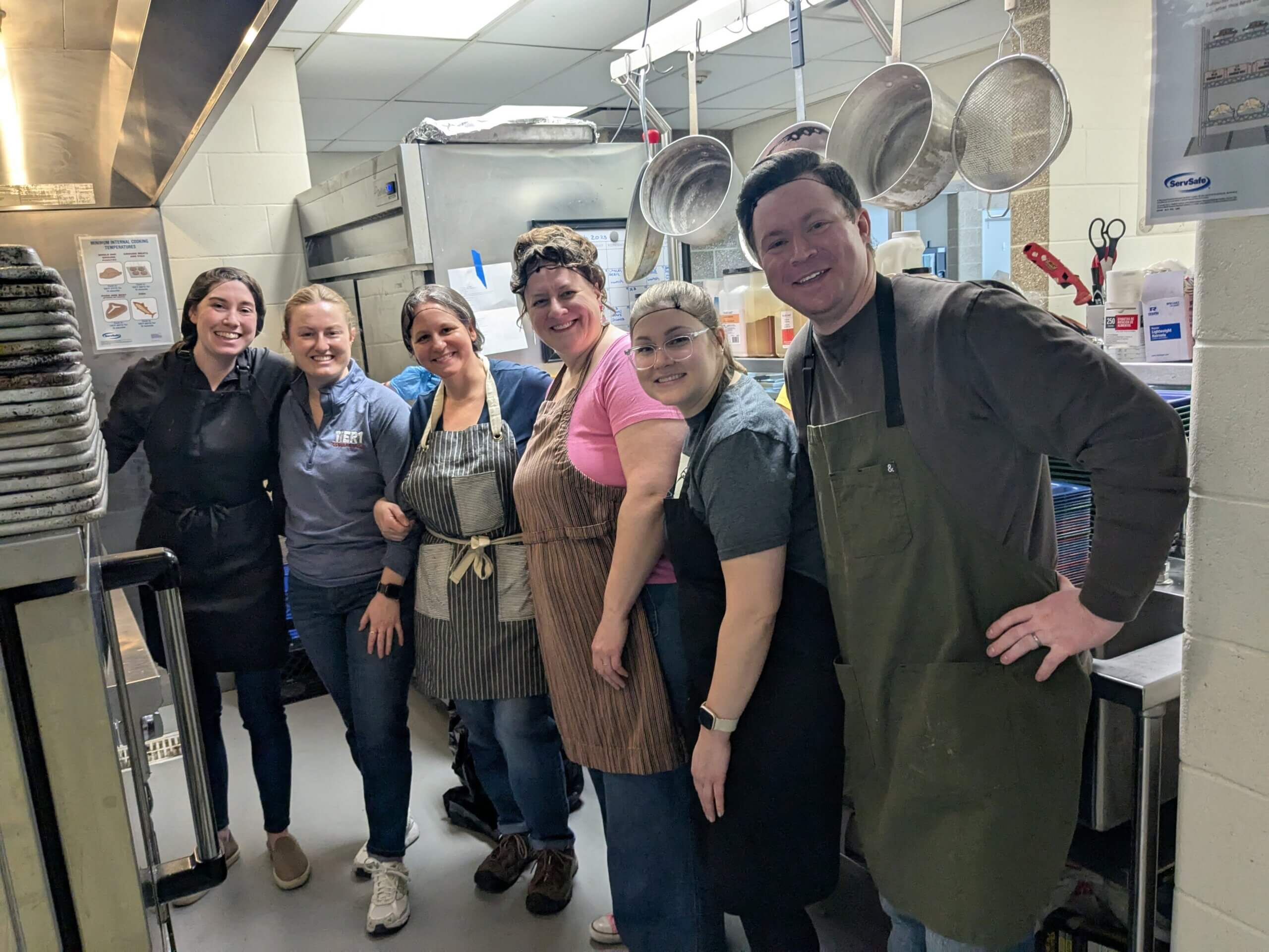 A group of people wearing aprons and hairnets to volunteer and serve food.