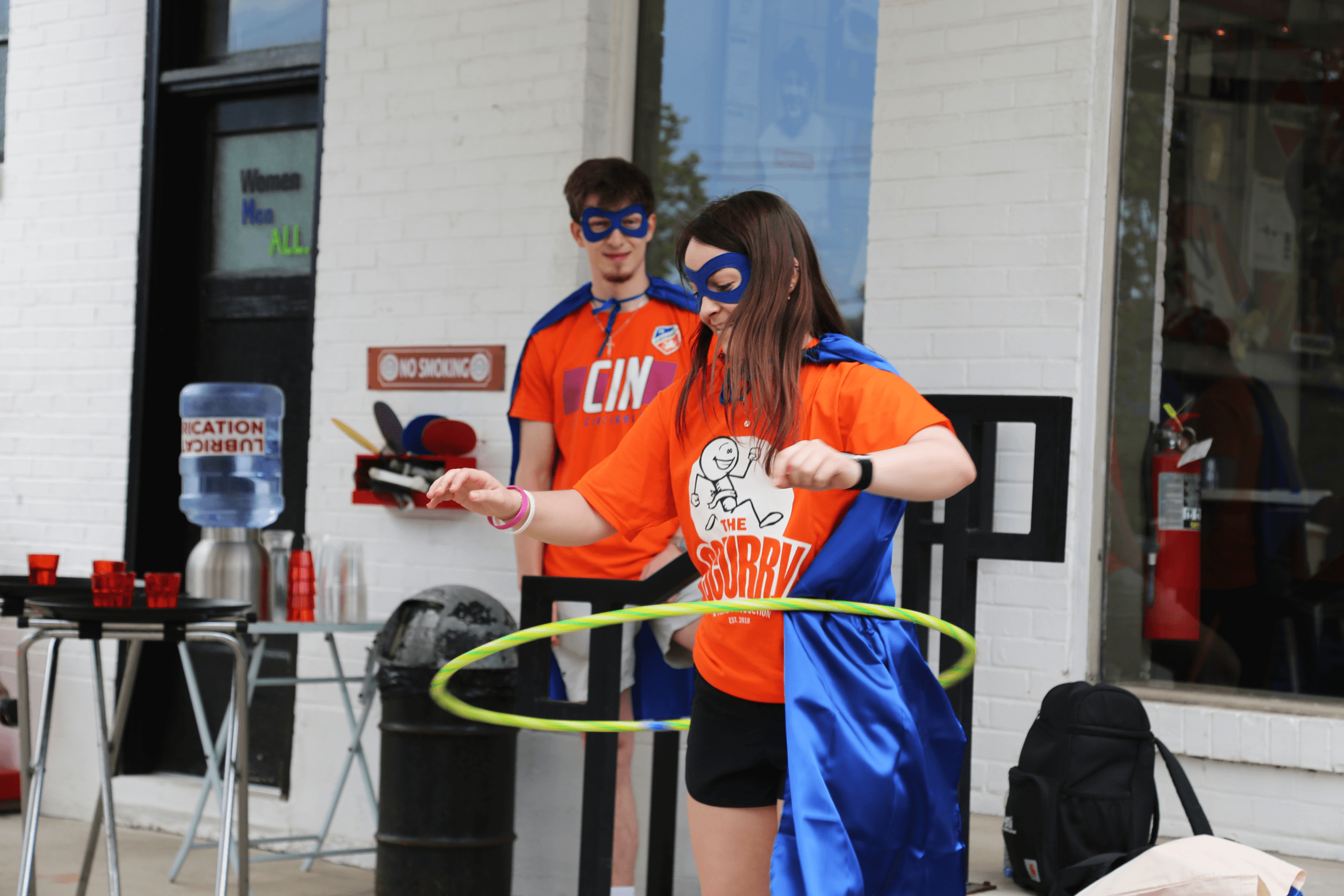 Girl in a superhero costume playing Hula-Hoop while her teammate watches.