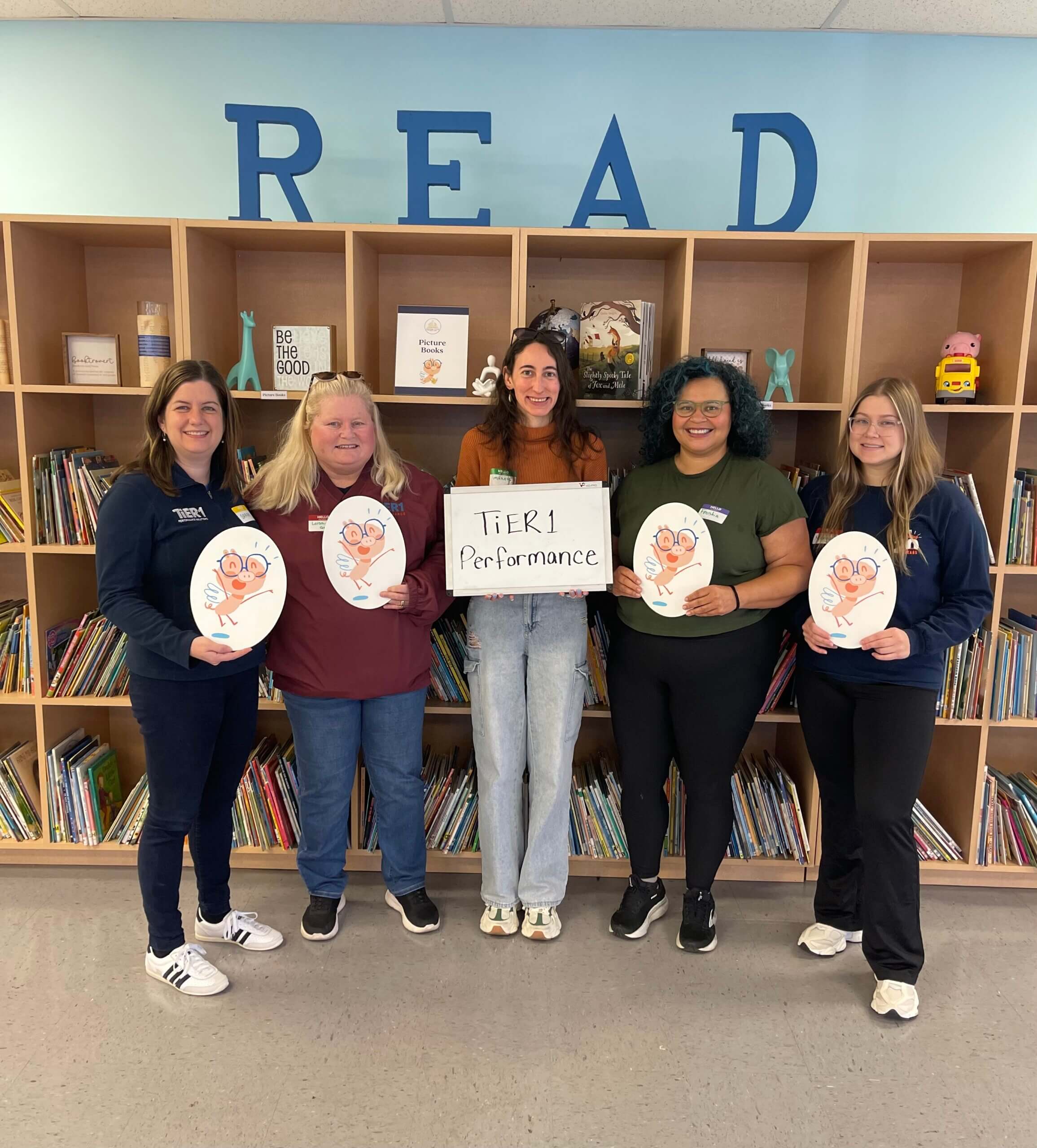 A group of women standing in front of a read sign and bookshelves full of books.